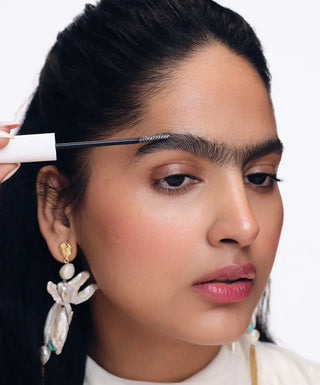 Woman applying mascara with a brush on a white background