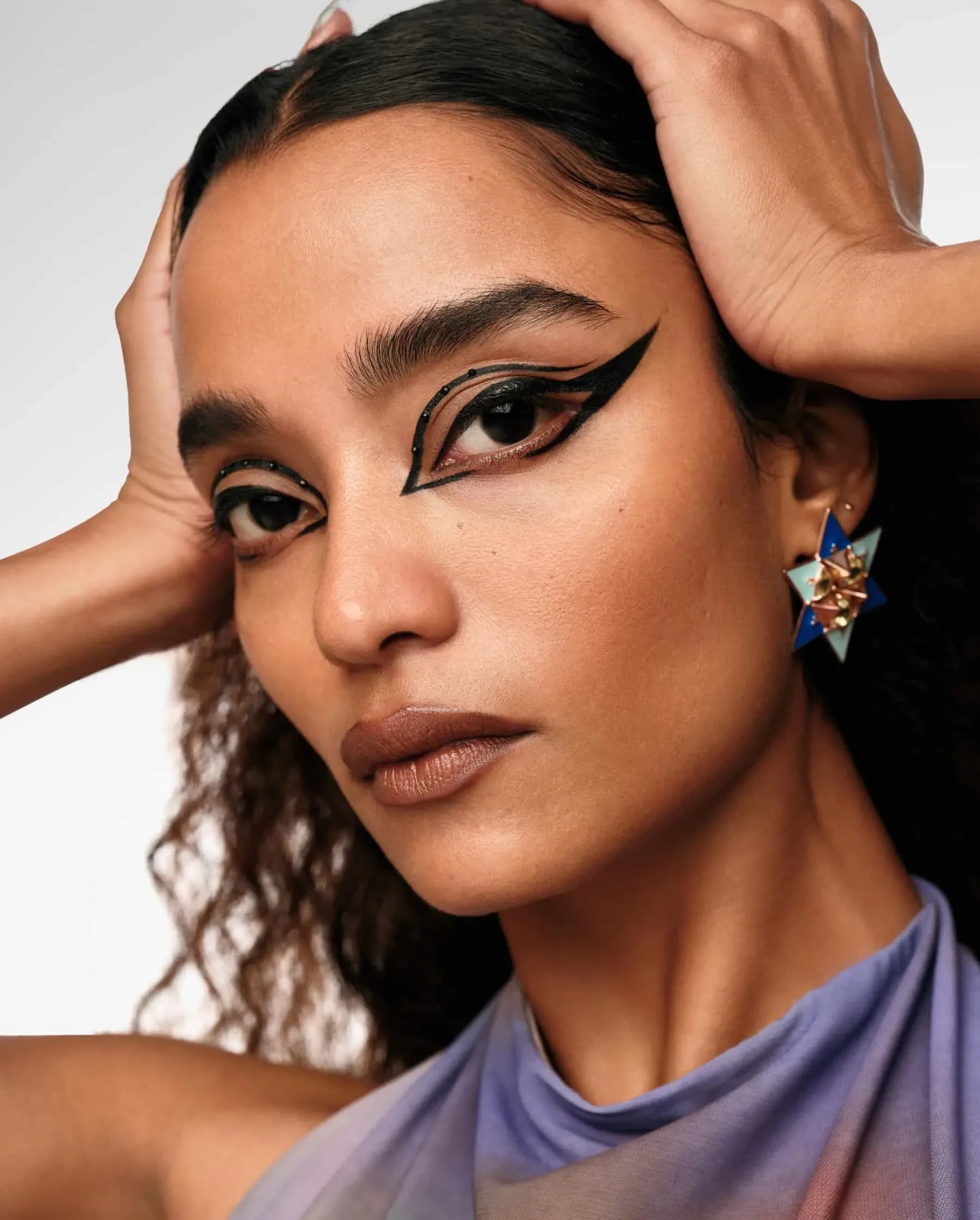 Woman with dramatic makeup and a stylish earring against a neutral background